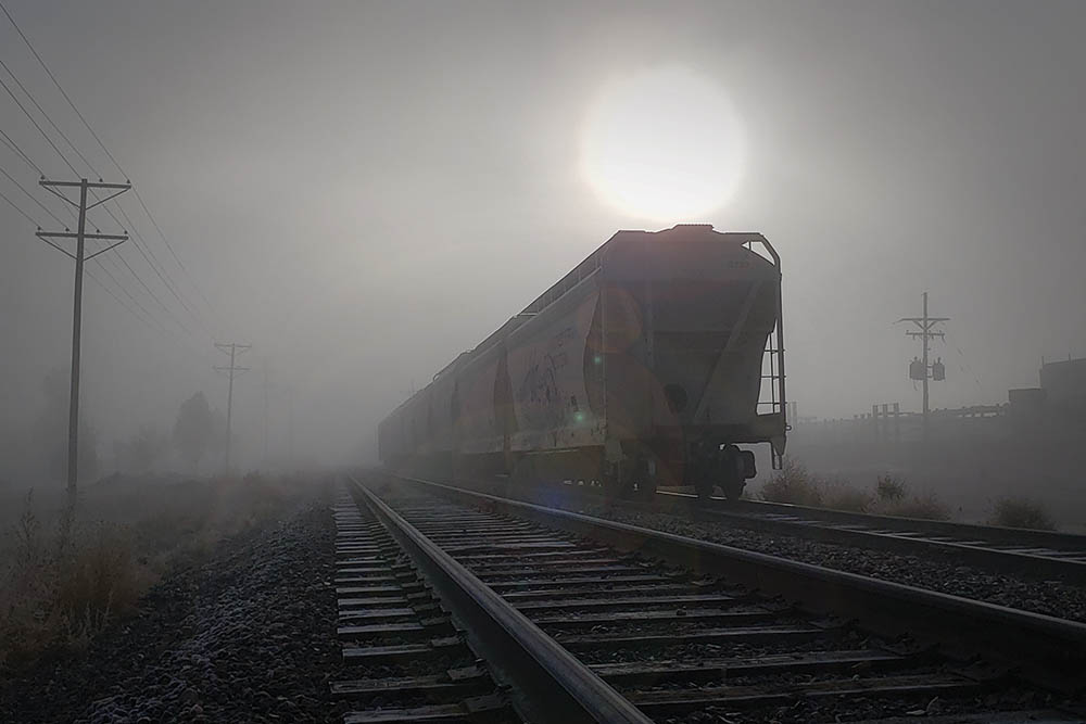 train tracks during the day in the fog with large rising sun